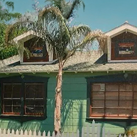 Green Craftsman home with two front dormers and dark-trimmed windows behind a white picket fence