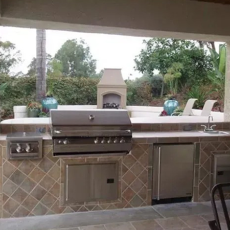 Tiled backyard kitchen with a built-in stainless steel grill, side burner and sink