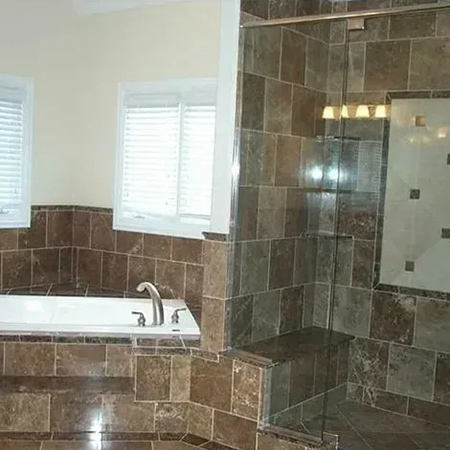 Bathroom with brown marble tile around a soaking tub and a glass-enclosed shower with a bench