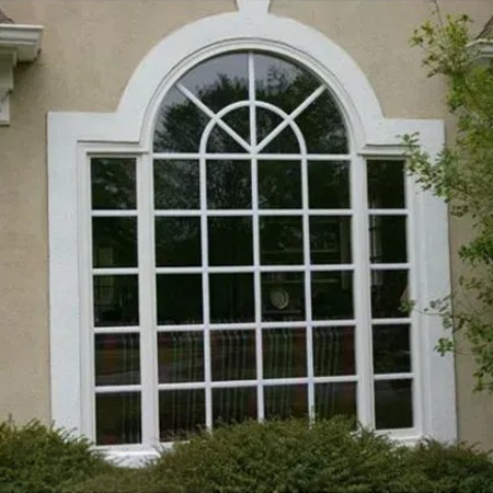 Arched window with white grid panes and trim set in a stucco wall