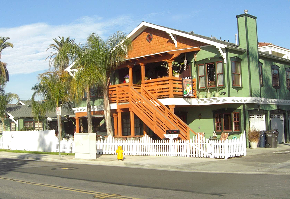 Two-story green Craftsman home with an orange wood exterior staircase and balcony