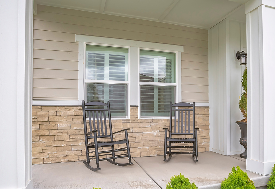 Double-hung windows with white shutters above a stacked-stone porch with rocking chairs