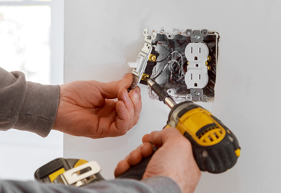Handyman wiring a new wall outlet and light switch with a cordless drill