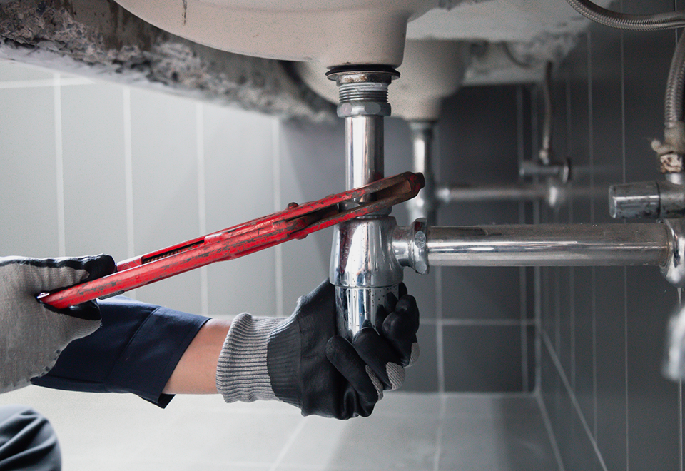 Plumber tightening a chrome sink drain pipe with a red pipe wrench