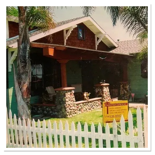 Craftsman bungalow with a river-rock front porch and a Handyman Express yard sign behind a white picket fence