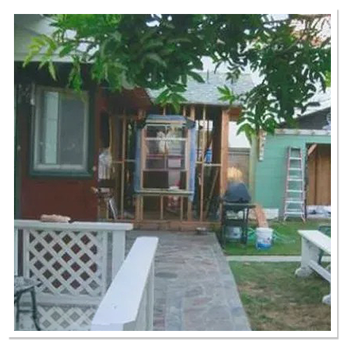 Backyard room addition being framed behind a patio with white lattice railing, a ladder and paint buckets