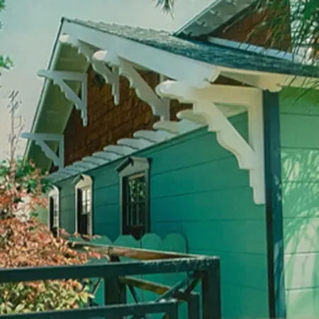 Side of a green Craftsman house with white eave brackets and cedar-shingle gables