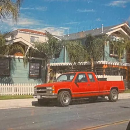 Red pickup truck parked in front of a remodeled two-story home with palm trees