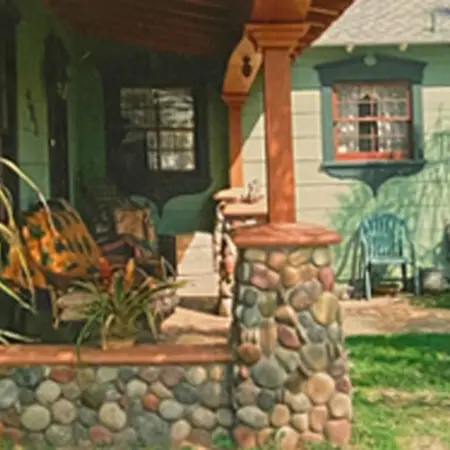 Covered porch with river-rock columns and a planter wall on a green Craftsman home